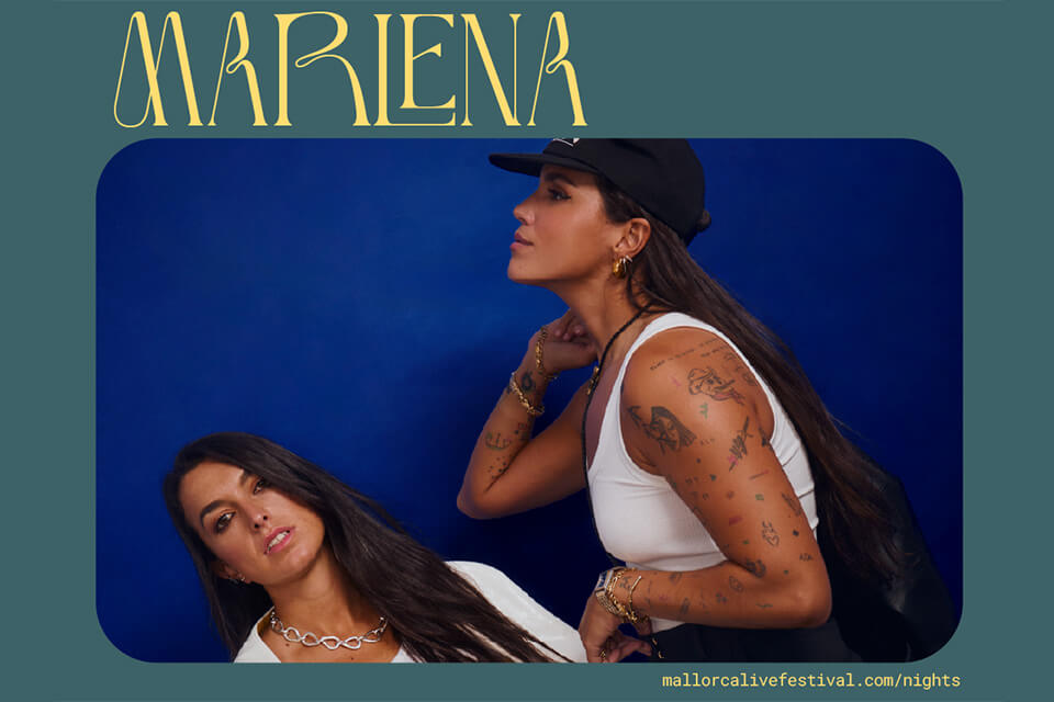 Two female performers posing against a blue background, one wearing a cap and white top