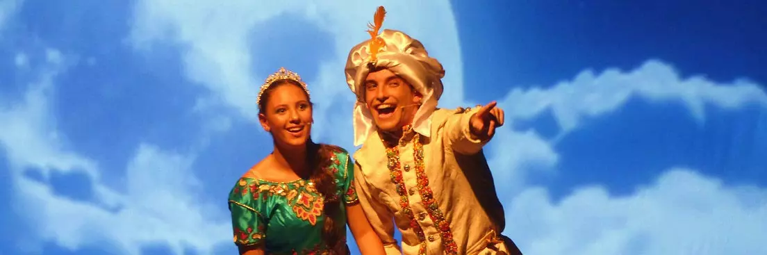 Scene from Aladdin the Musical showing two performers dressed as Aladdin and Jasmine against a blue sky backdrop.
