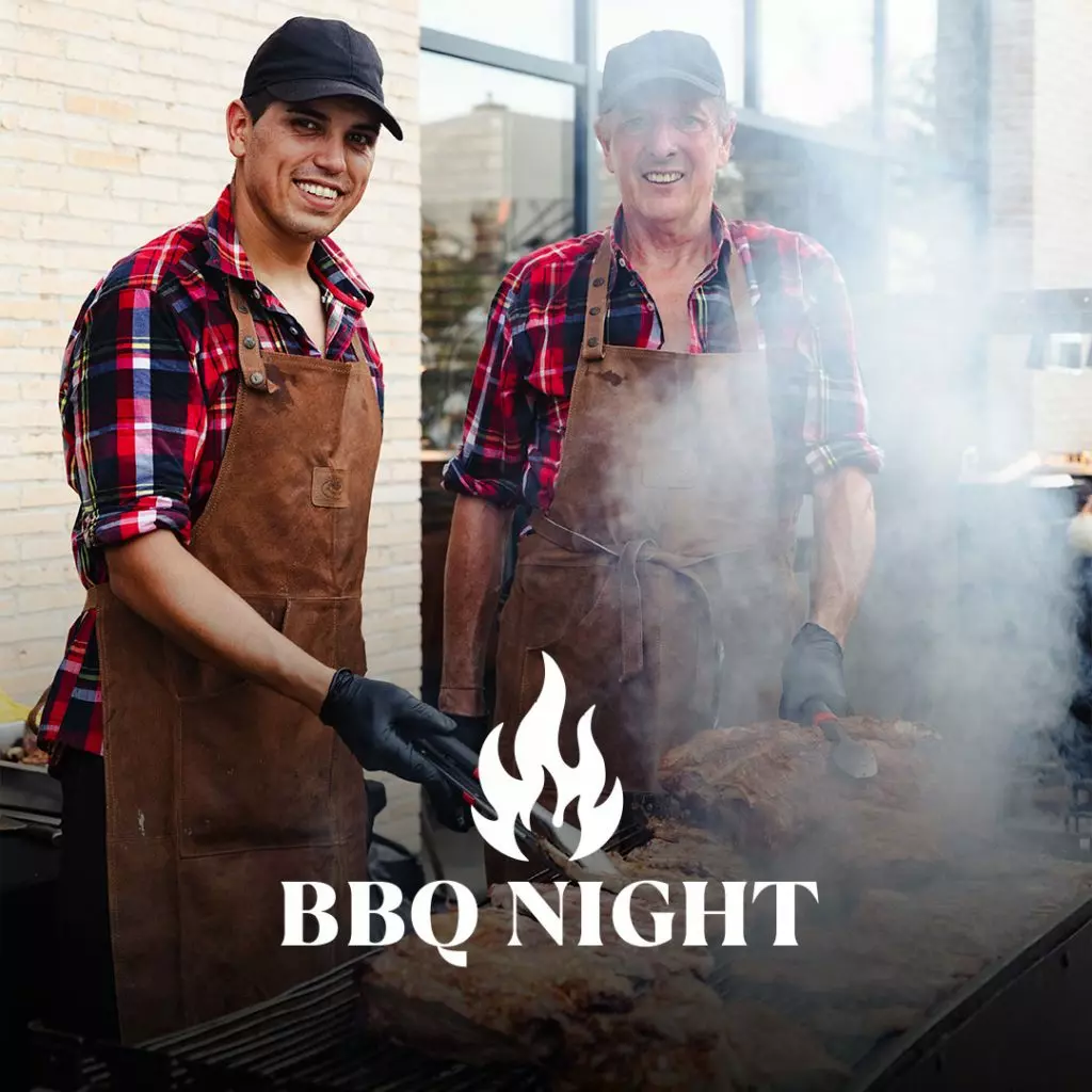 Two people wearing aprons and plaid shirts grilling meat at an outdoor BBQ station with smoke rising from the grill.