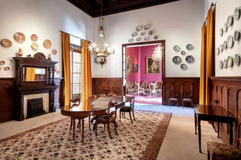 Historic interior room of Can Balaguer with wooden furniture and chandelier.