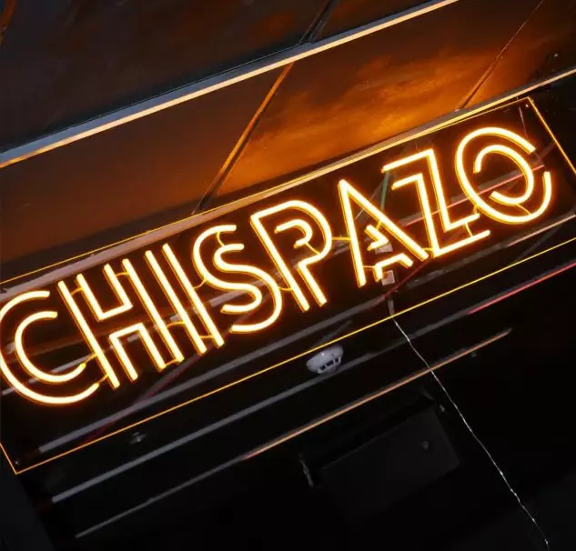 Neon sign reading “CHISPAZO” in bright orange letters at a bar or club.
