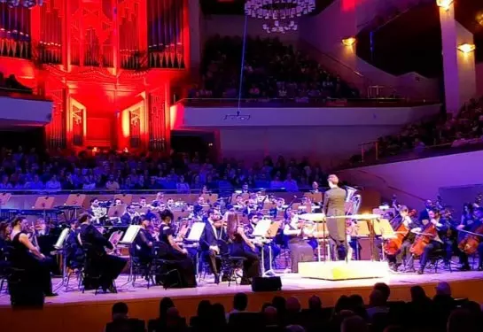 Orchestra performing film music on stage at Auditorium Palma under colourful lighting.