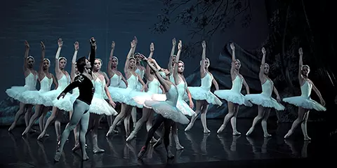 Ballet dancers performing Swan Lake, with the corps de ballet in white tutus on a dark, atmospheric stage.