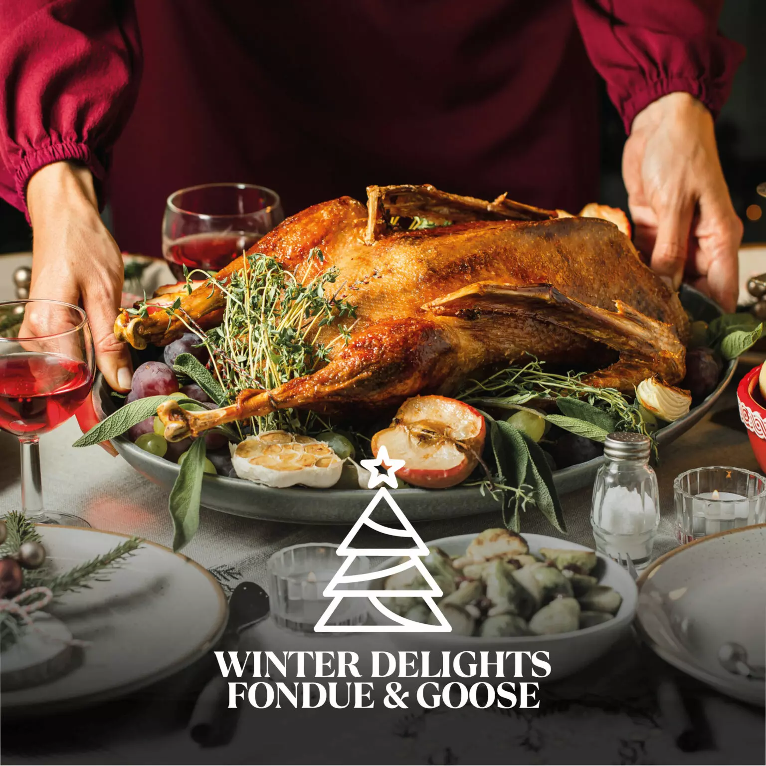 A roasted goose served on a festive table with herbs, apples, and winter decorations, with hands adjusting the platter and glasses of red wine nearby.