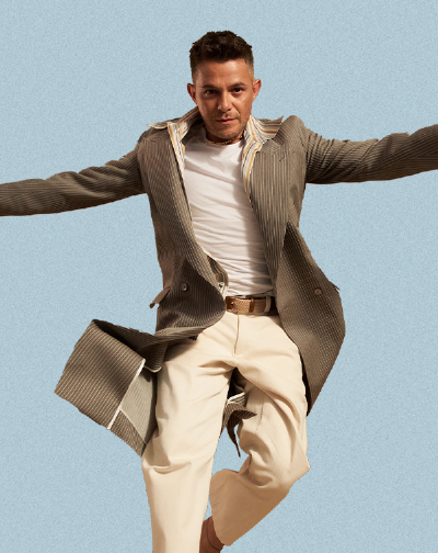Promotional photo of Alejandro Sanz jumping with arms extended against a light background.