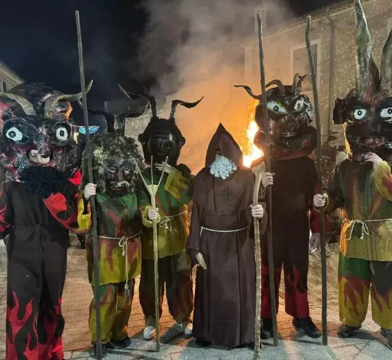 People wearing traditional devil masks holding staffs during a fire run at night