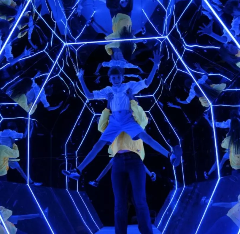 Child in a mirrored room with blue light installations.