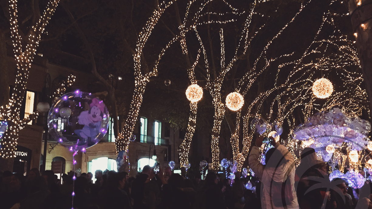 Nighttime street filled with Christmas lights decorating the trees and a crowd of people.