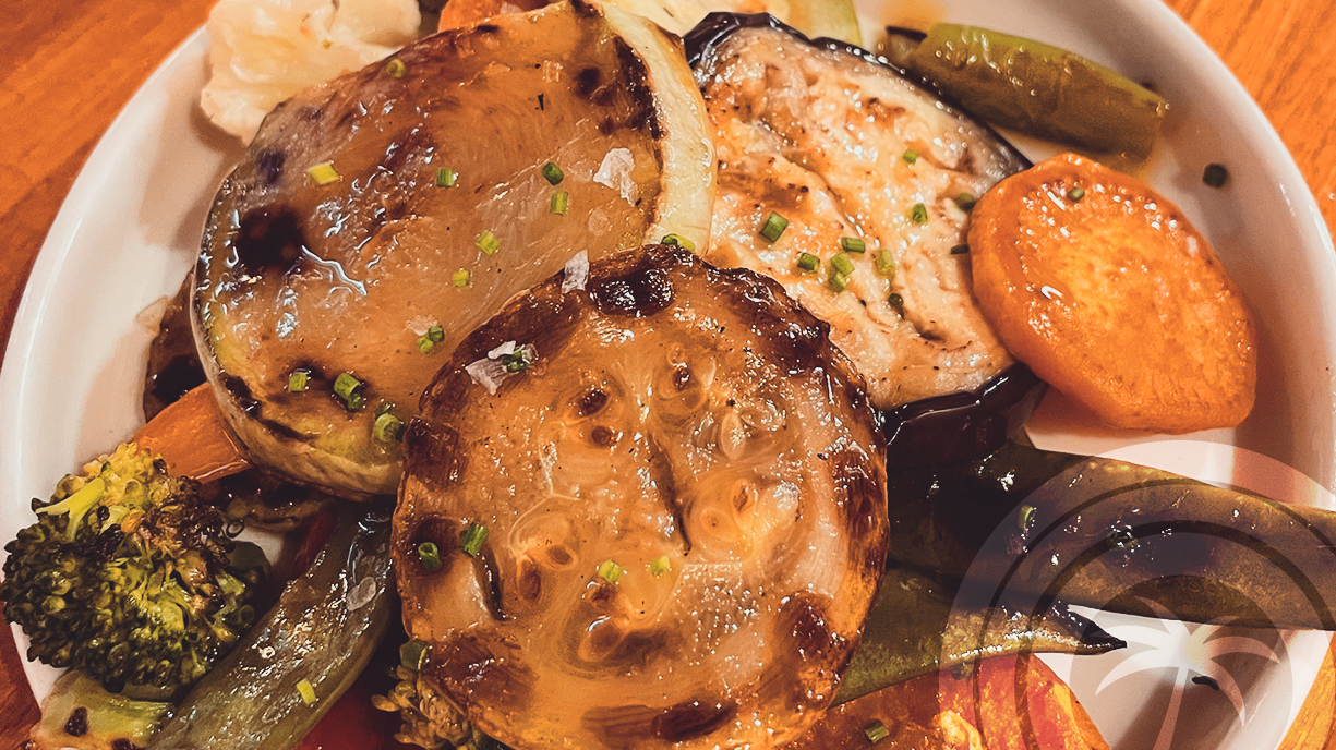 Grilled seasonal vegetables including aubergine, onion, sweet potato, and broccoli, served on a white plate.
