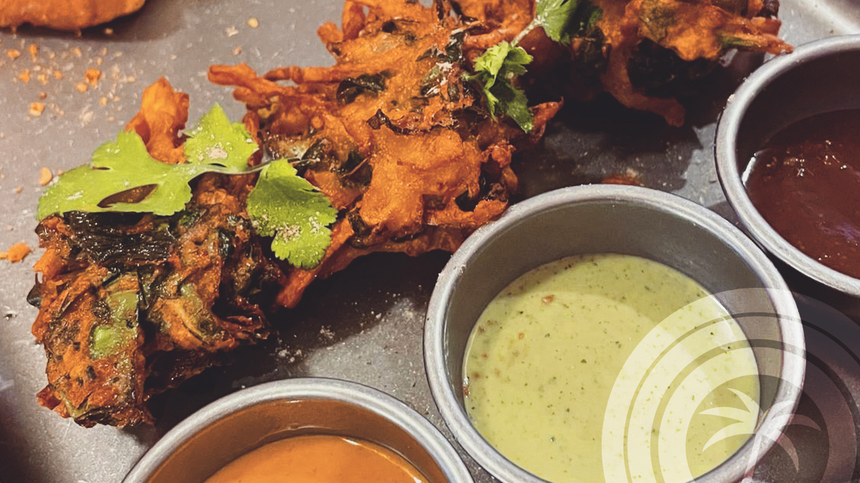 Fried fritters with cilantro leaves and three dipping sauces in metal bowls