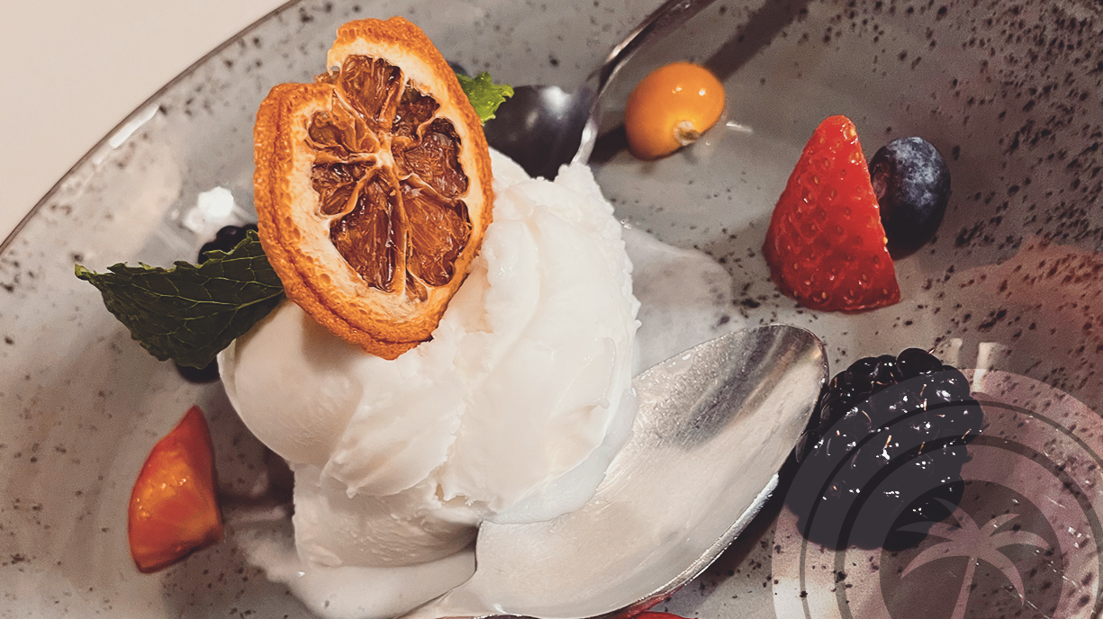 White sorbet served in a bowl, topped with a dried citrus slice and mint, with assorted berries on the side.
