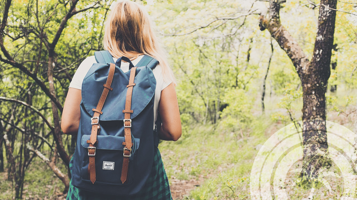 A woman with a backpack walking along a forest trail during a hike.