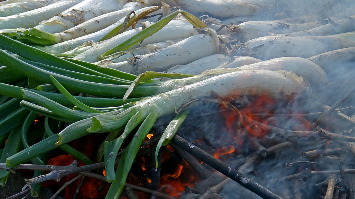 Calçots placed directly over an open fire, with smoke rising around them.
