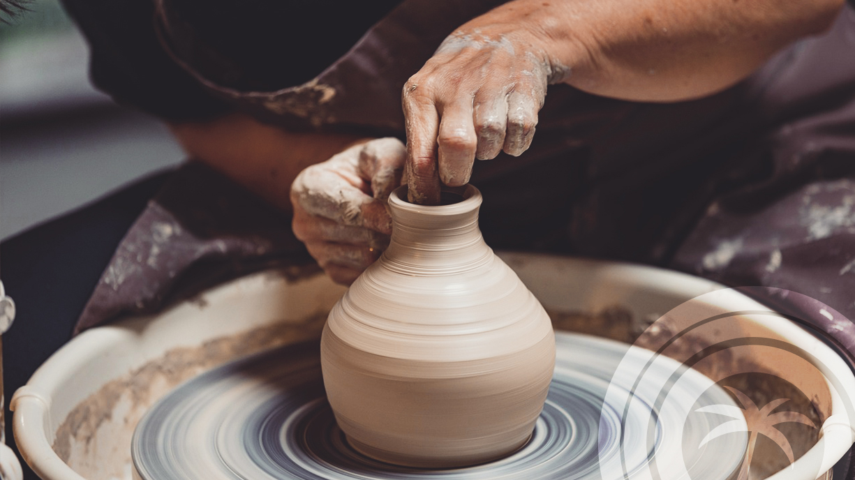 Person shaping a clay pot on a spinning pottery wheel with their hands.