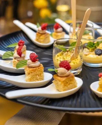 Small dessert bites with raspberries and cream served on spoons alongside glasses of custard