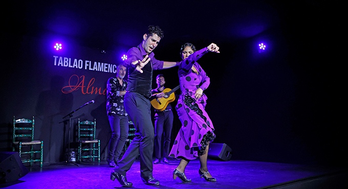 Flamenco dancers performing on stage with purple lighting.