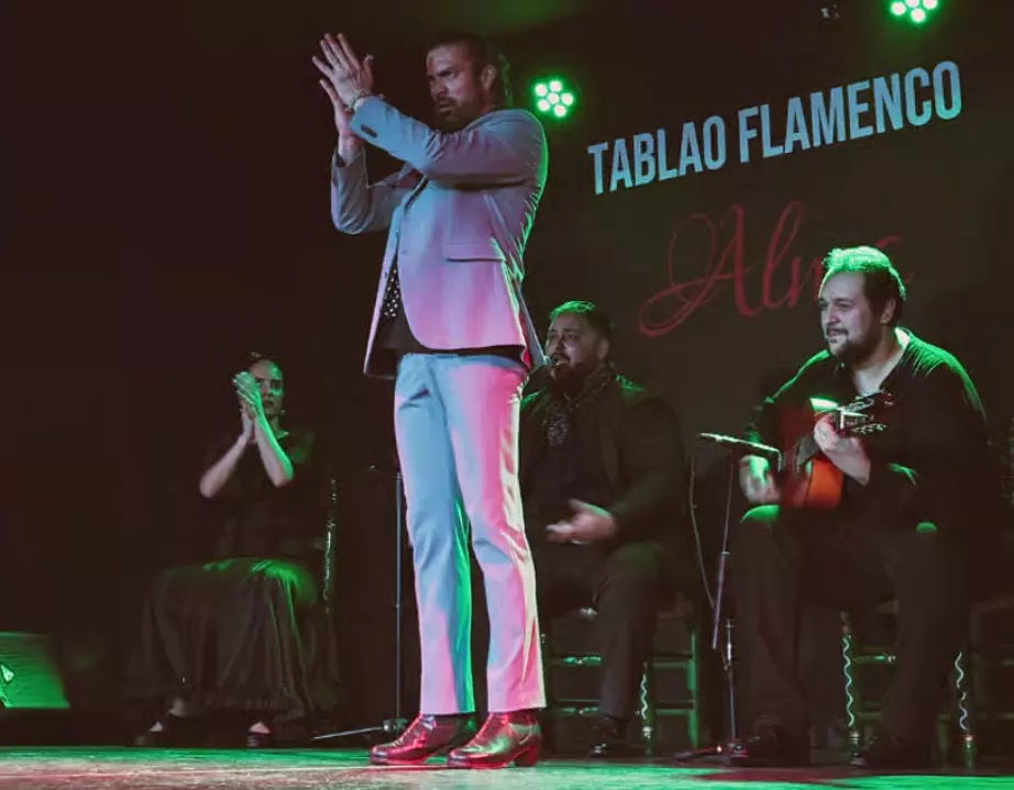 A flamenco dancer performing on stage while musicians play guitar and provide rhythmic clapping behind him.