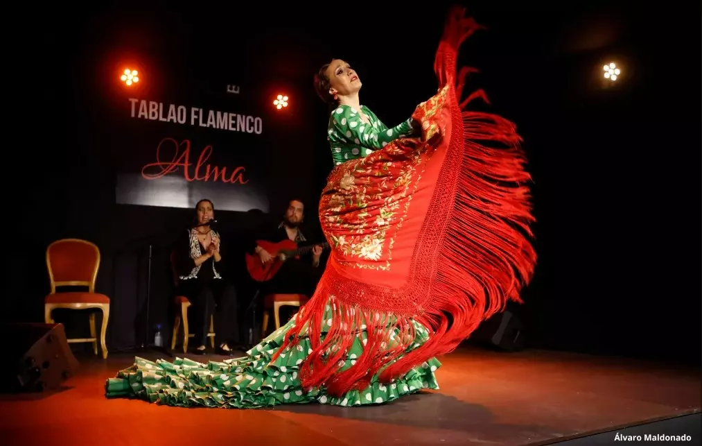 Flamenco dancer in a green polka-dot dress performing with a red shawl on stage at Tablao Flamenco Alma in Palma, accompanied by live musicians.